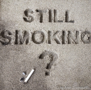 The question 'Still Smoking?' are block printed in sand with a question mark and a cigarette butt nearby.  Best Buy this Image Art  at http://jo-ann-tomaselli.artistwebsites.com/featured/still-smoking-image-art-jo-ann-tomaselli.html